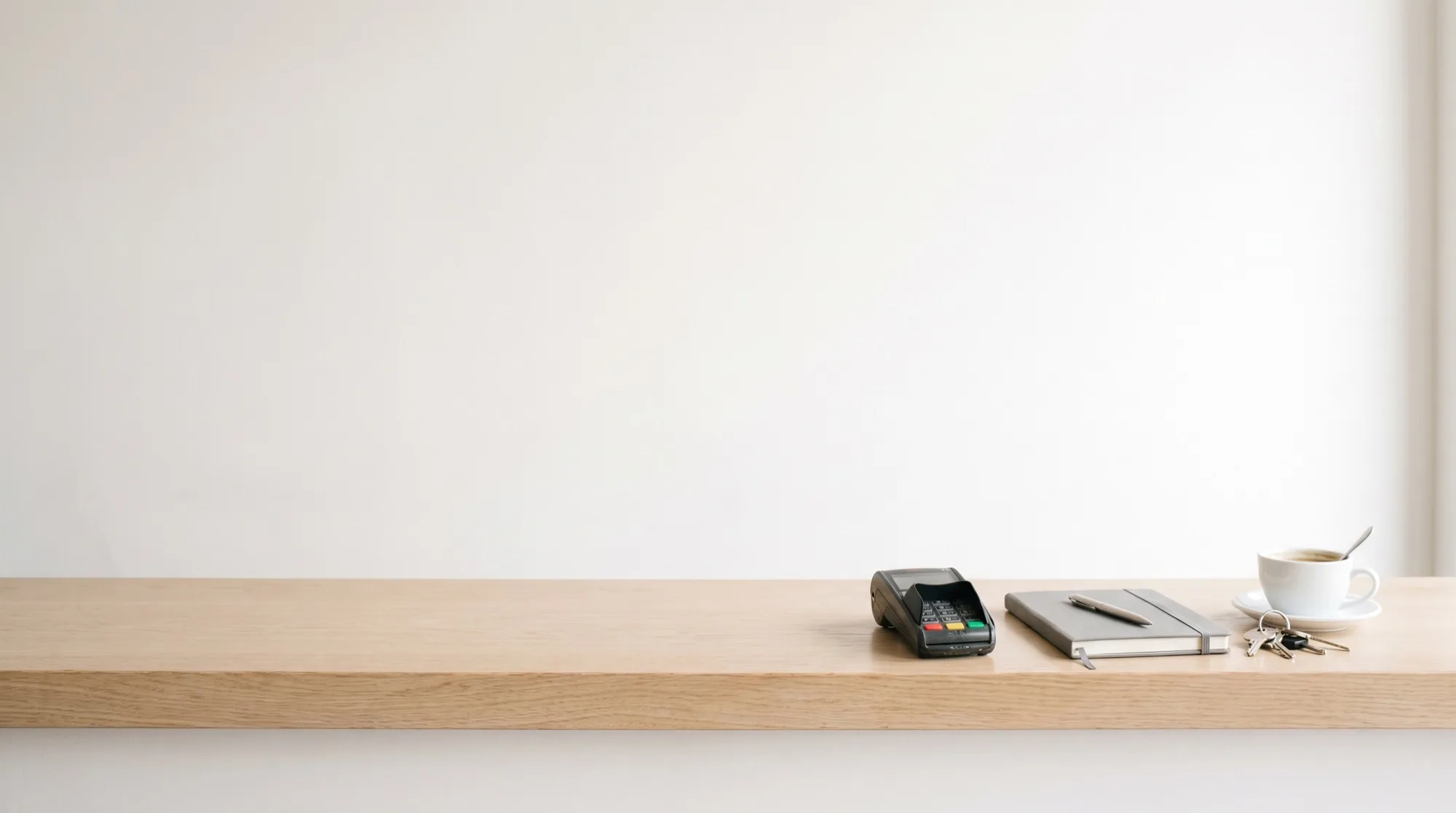 A small business counter with a card reader, a notebook, keys and a coffee, and a phone standing on it showing Rumore.